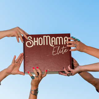 A person-centered lifestyle shot showing multiple hands holding a square box with the brand name 'Shomama Elite' printed on it, set against a clear blue sky.